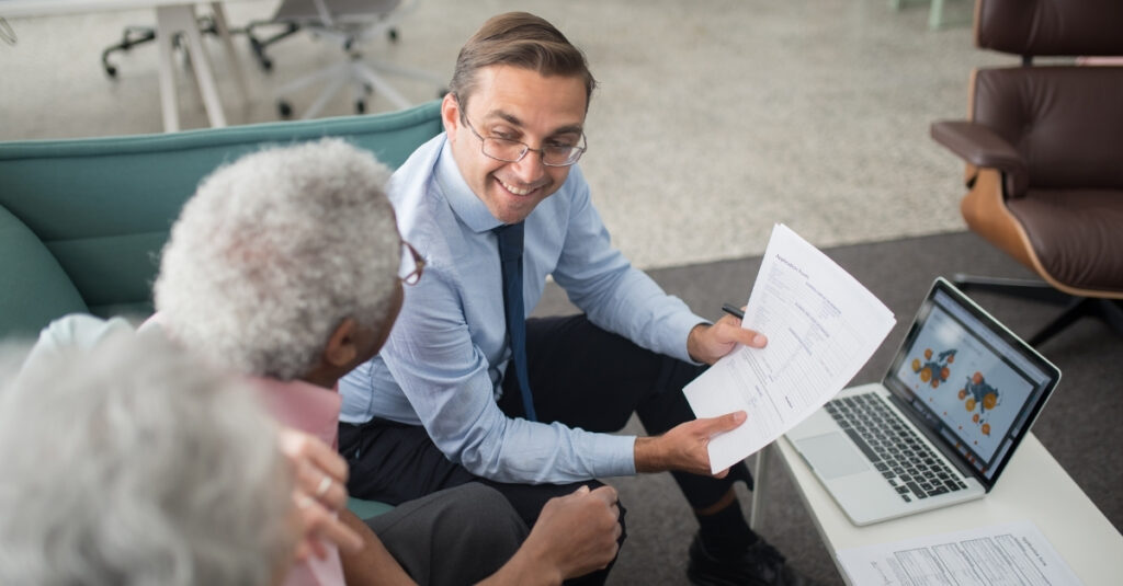 A financial advisor smiles while discussing documents with an elderly couple, highlighting proactive communication and personalized financial planning support.